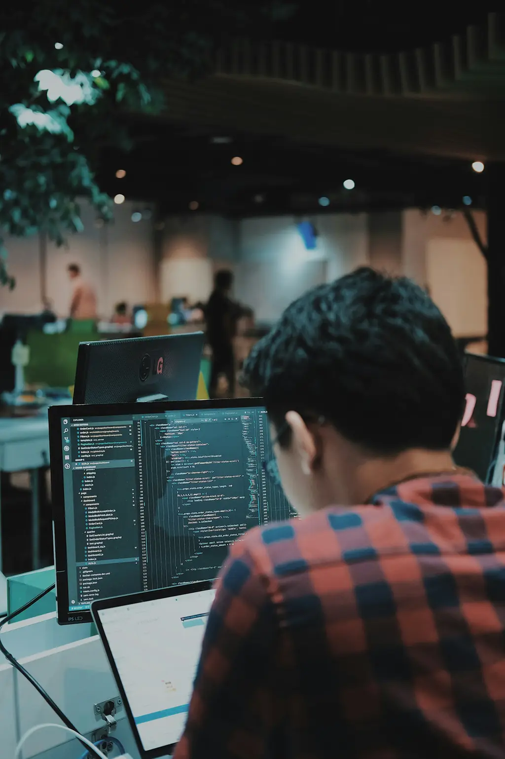 A developer writing code on a large monitor in an open office