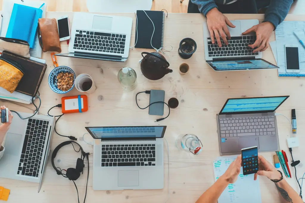Top-down view of a shared desk with laptops, a phone and hands at work